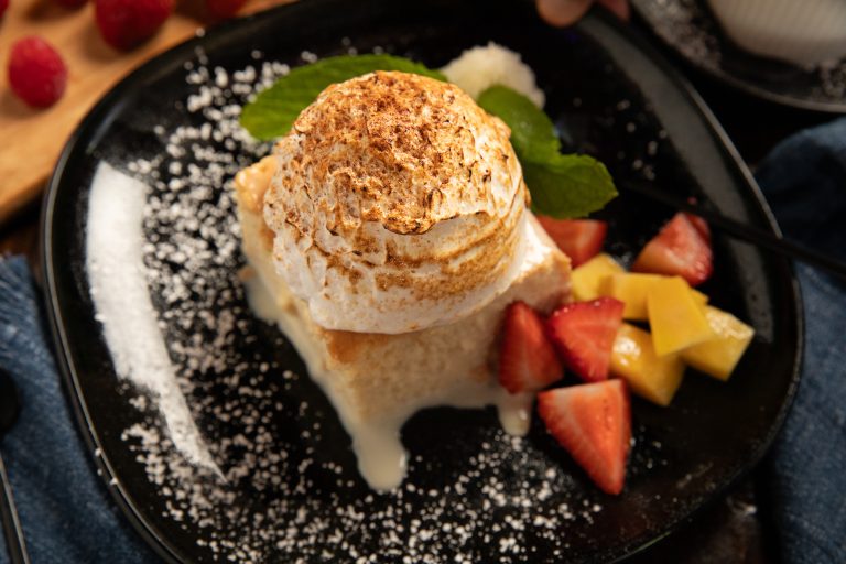 Tres Leches with fruit on side set on black plate sprinkled with powdered sugar.