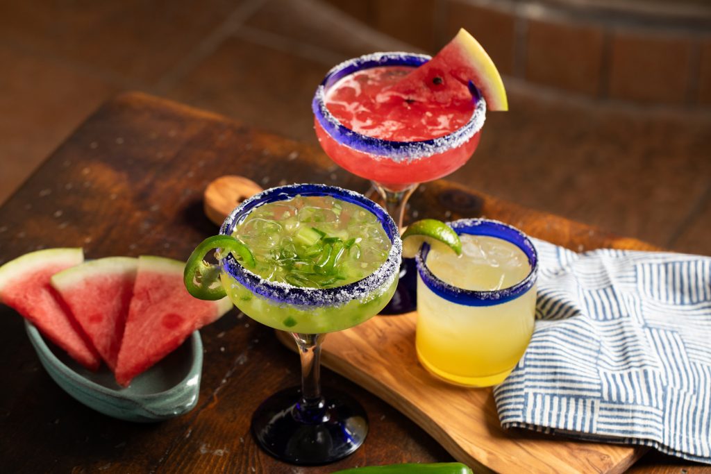 Watermelon slices on wooden table with Jalapeno margarita, strawberry margarita and classic margarita