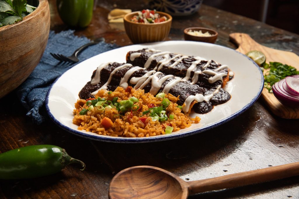 Table with blue napkin and enchiladas with mole sauce.