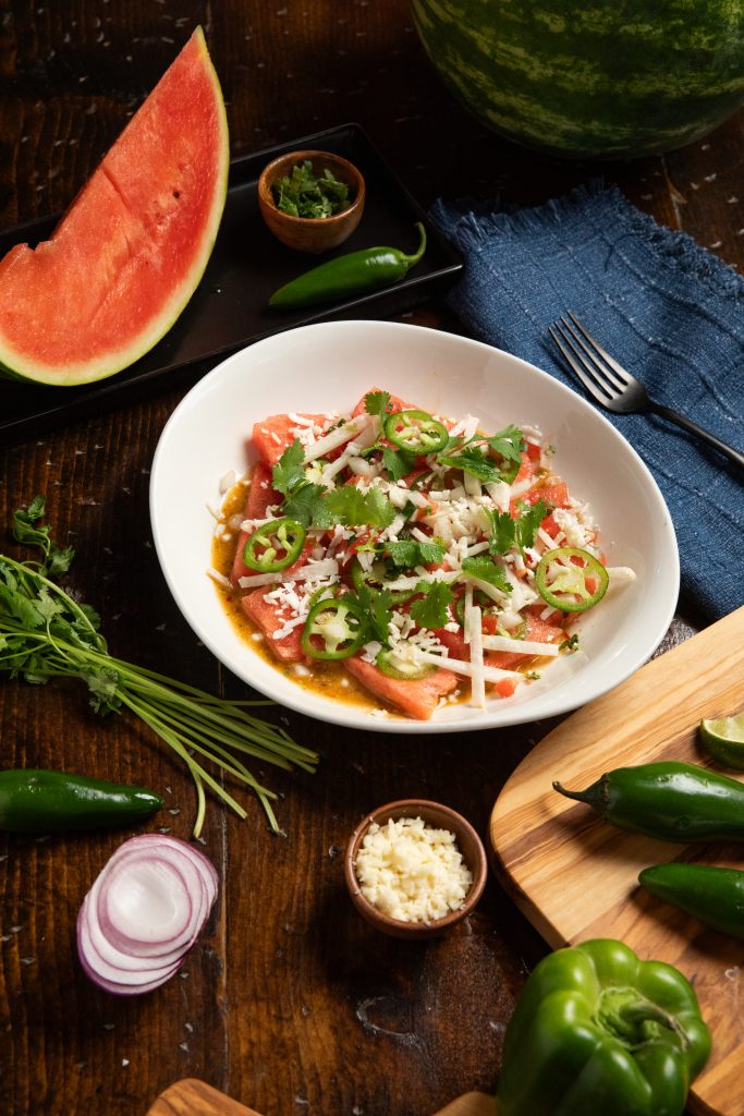 Watermelon Jalapeno Salad set on wooden table with Watermelon slice, onion and jalapenos