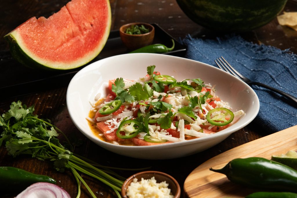 White bowl holding watermelon jalapeno salad with large slice of watermelon and whole jalapeno