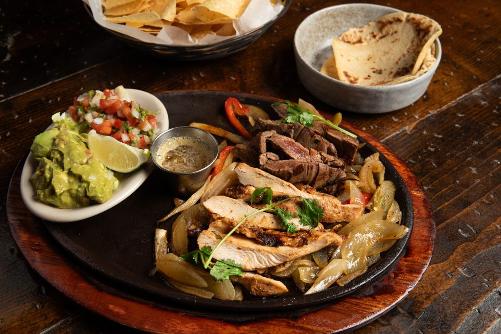 Fajitas on wooden platter, flour tortillas, guacamole