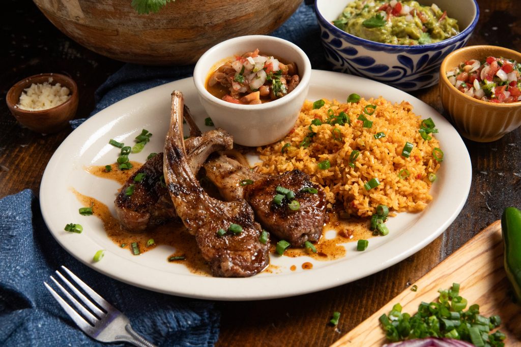 Classic plate of lamb chops with rice and beans. Guacamole in background.