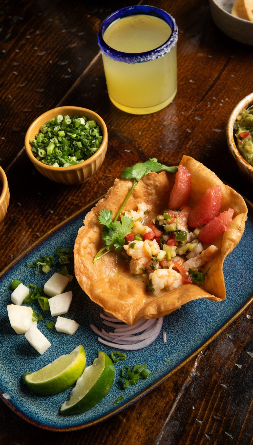 Cerviche in Taco shell set on blue plate with limes and margarita.