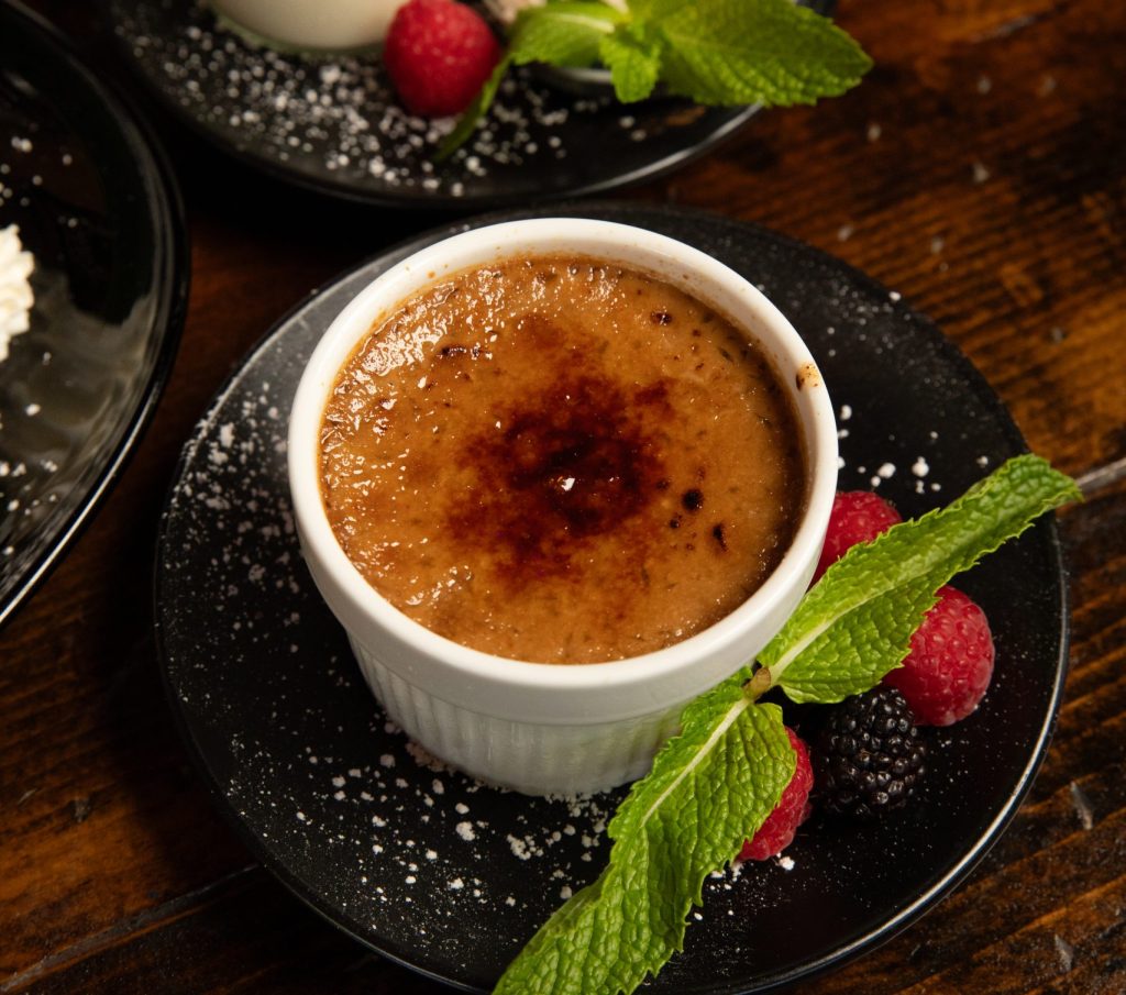 Classic Flan with mint and raspberry garnish. In background is Pina Colada dessert.