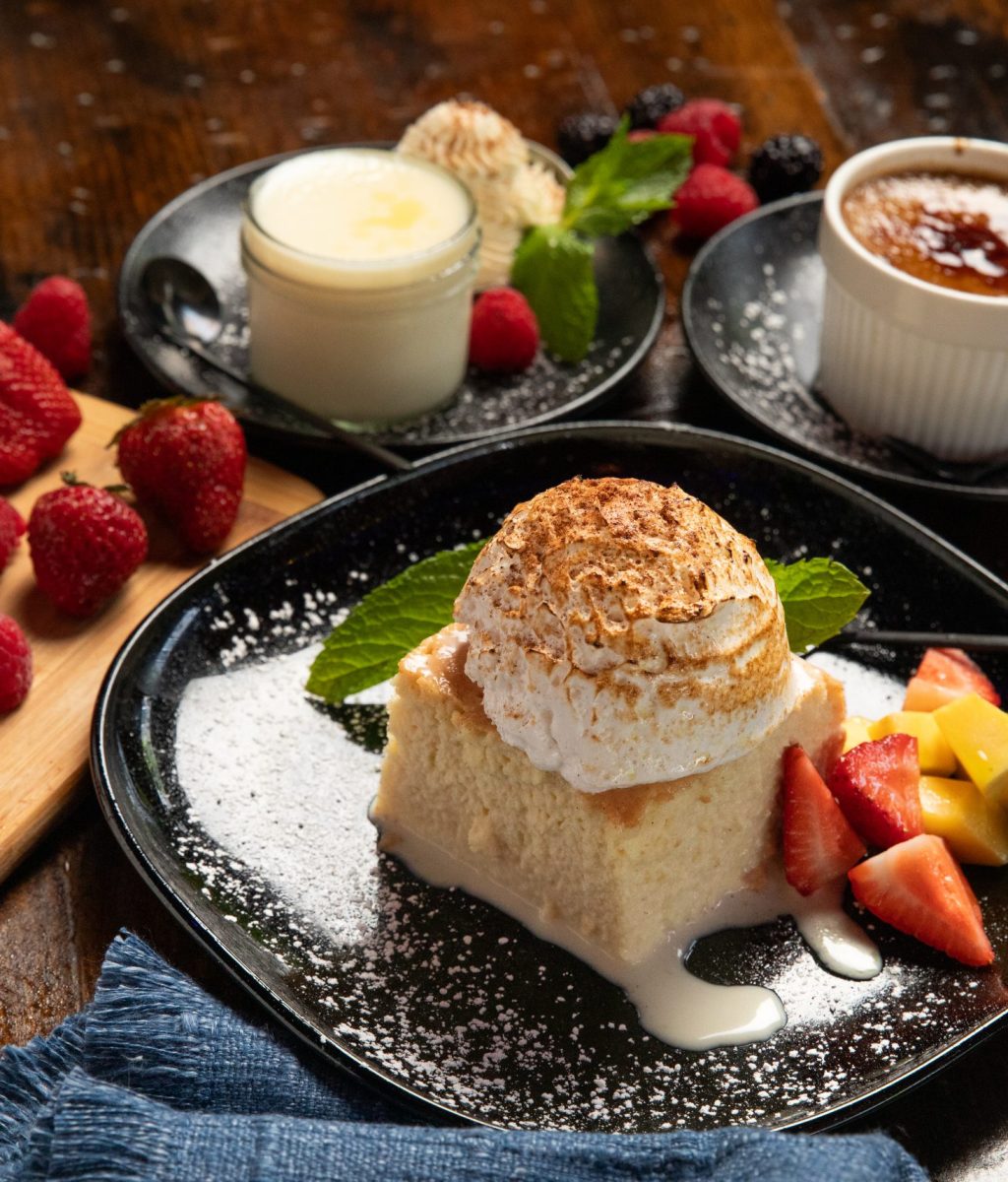 Table set with black plate holding tres leches, flan and pina colada desserts. Garnished with raspberries.