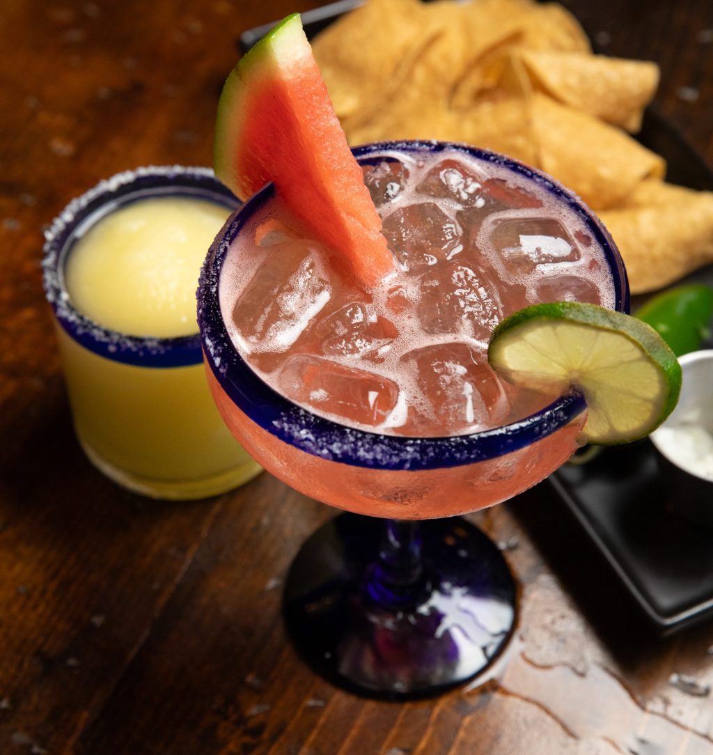 Frozen classic margarita on wooden table with a watermelon margarita and chips