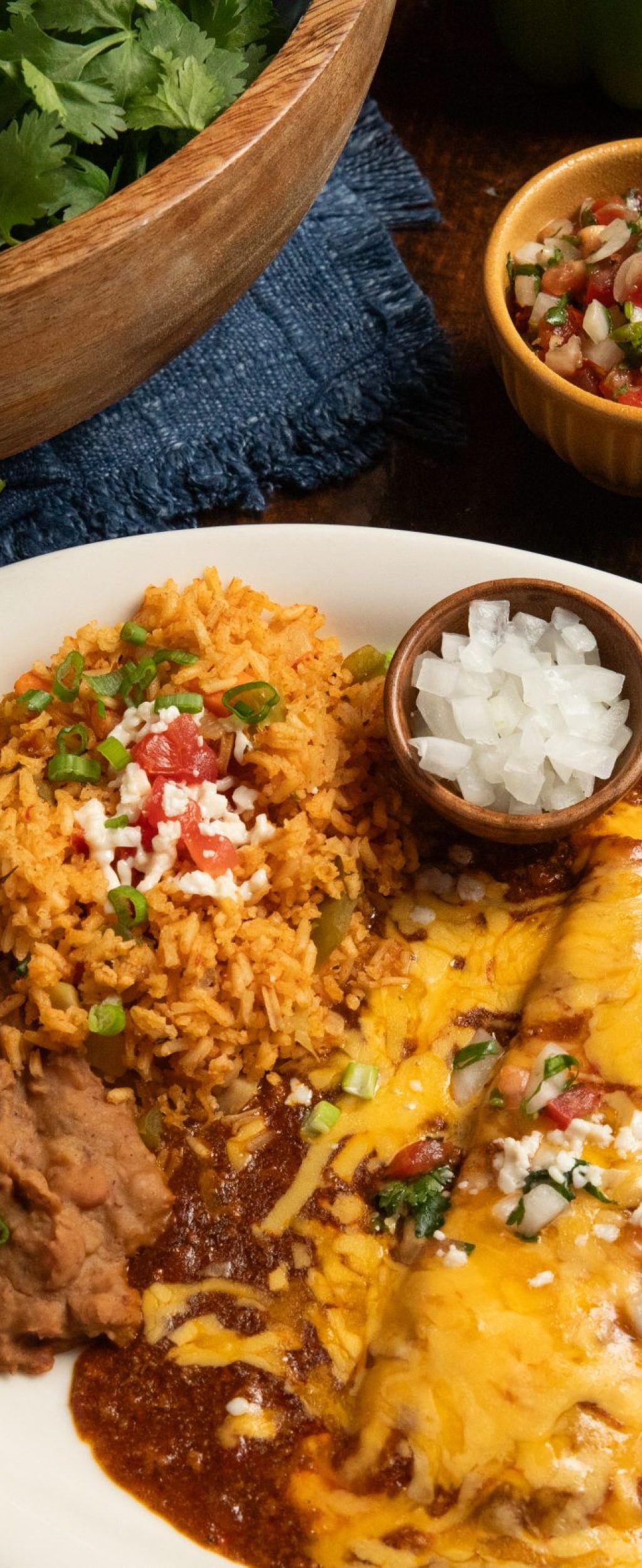 Cheese enchiladas on wooden table. Cilantro and others spices set around plate.