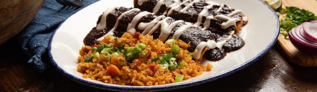 Table with blue napkin and enchiladas with mole sauce.