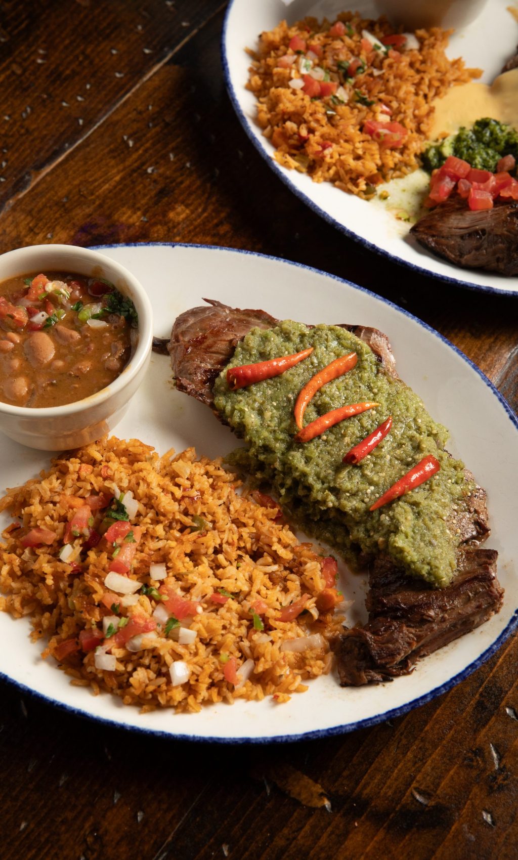 Plate of steak covered with green carne together with rice and beans on wooden table