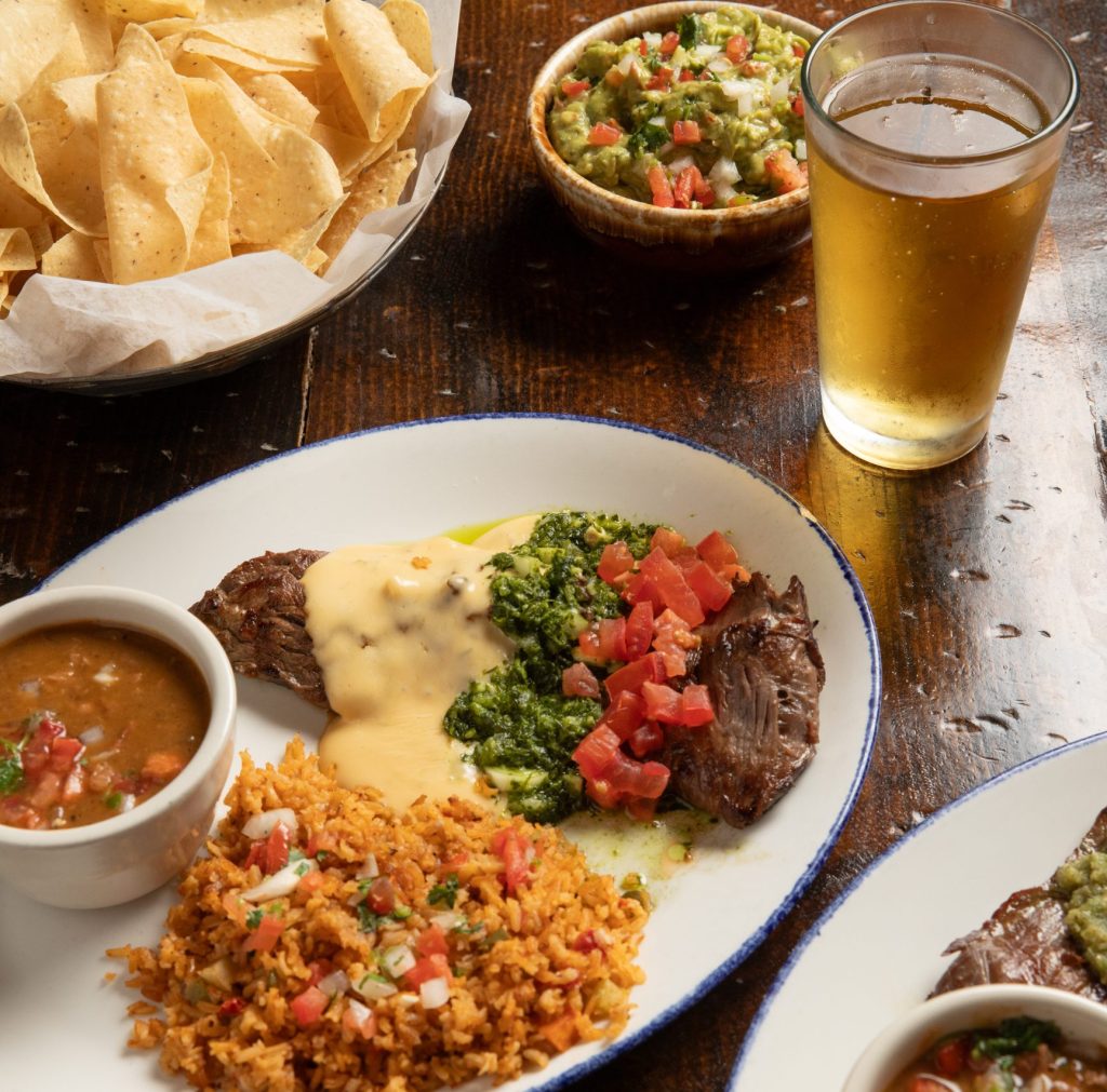 Table with chips and beer along with beef dish rice and beans.