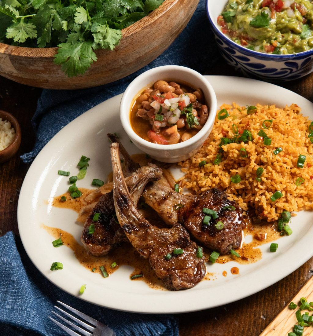 Classic lamb chops with rice and beans accompanied by guacamole on wooden table