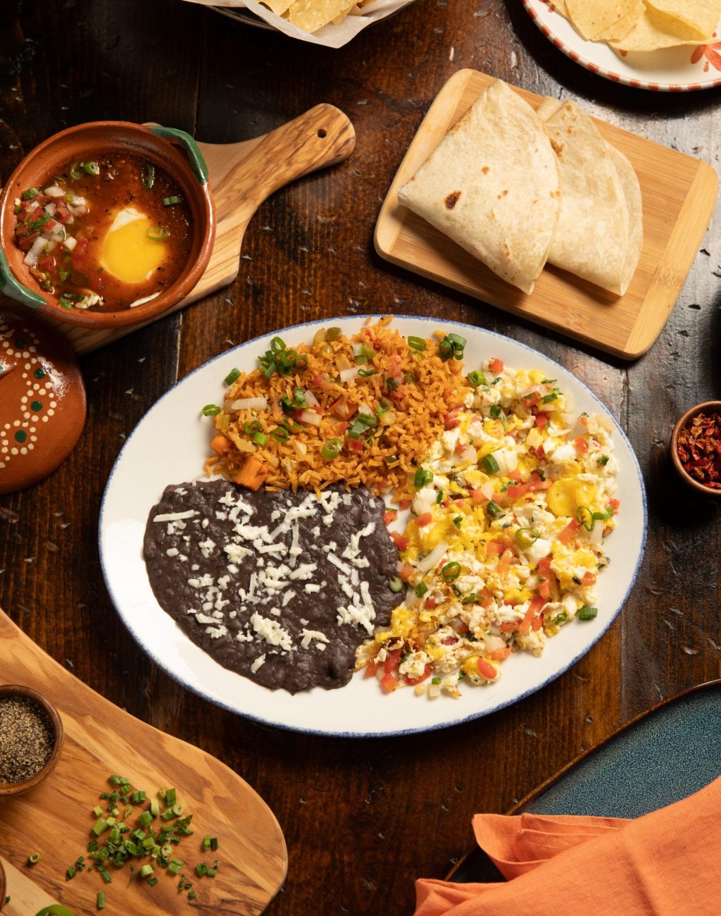 Table set with plate of eggs scrambled, tortillas, beans, rice and herbs.