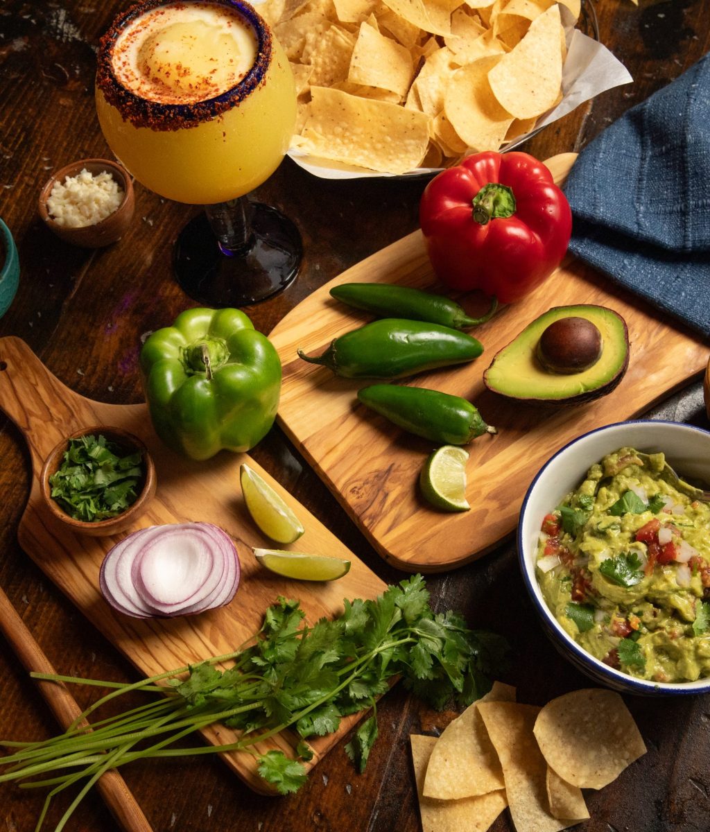 Spices, bell peppers, avocado, slice onion with chips, guacamole and margarita on wooden table.