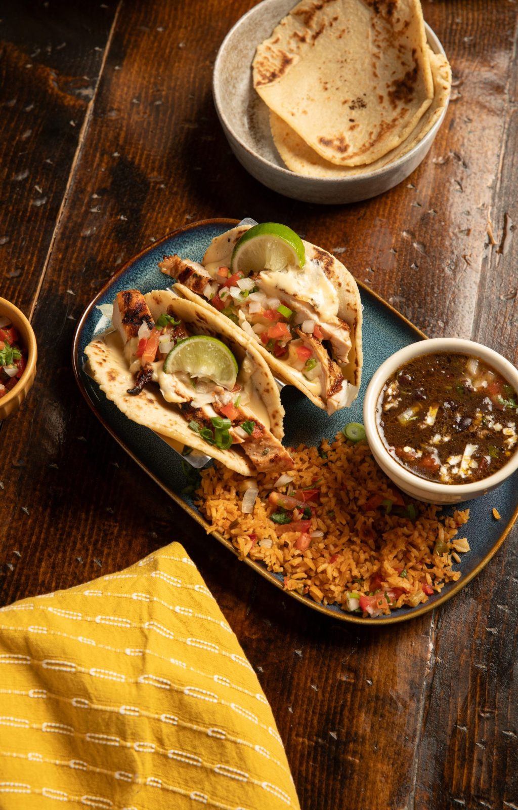 Soft Tacos, beans and rice with flour tortillas on wooden table with yellow napkin as accent